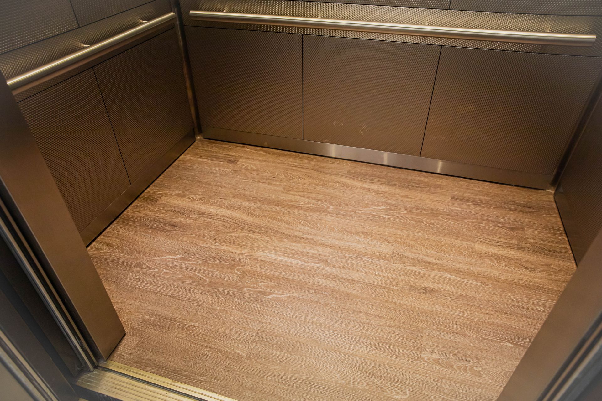 Empty elevator interior with wood-pattern floor and metallic walls.