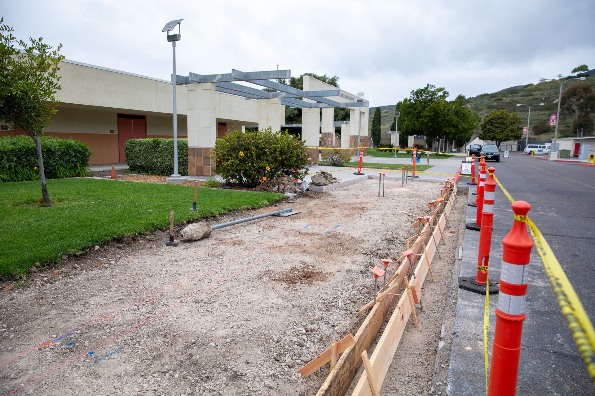 Roadside construction area with gravel trench, orange traffic cones, and buildings on the left