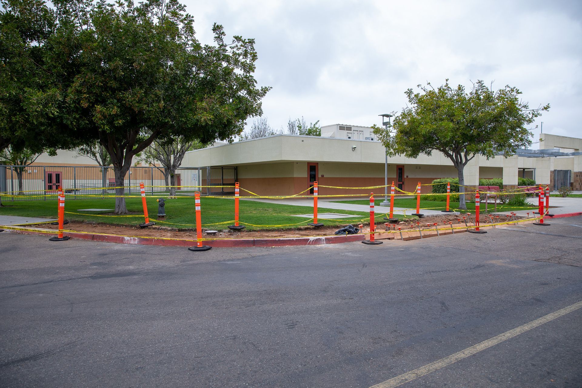 Orange safety fencing surrounds a damaged curb and sidewalk in front of a white house and trees.