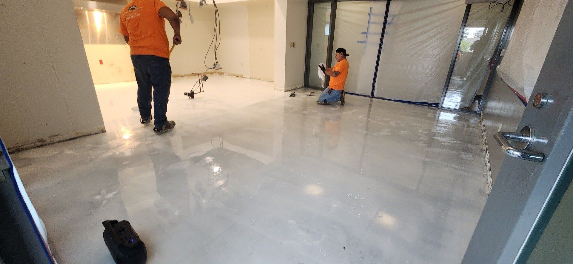 Two men in orange shirts are working on a white floor