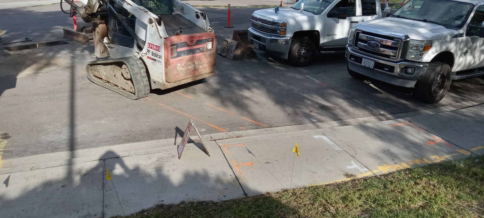 A bobcat is being used to dig a hole in the sidewalk.
