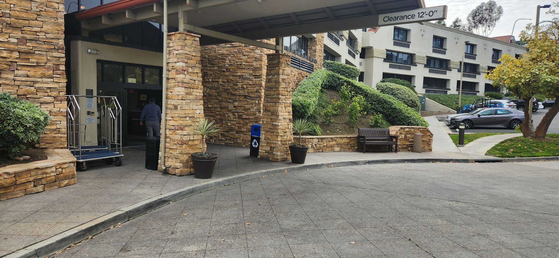 A man is standing in front of a hotel with a luggage cart.