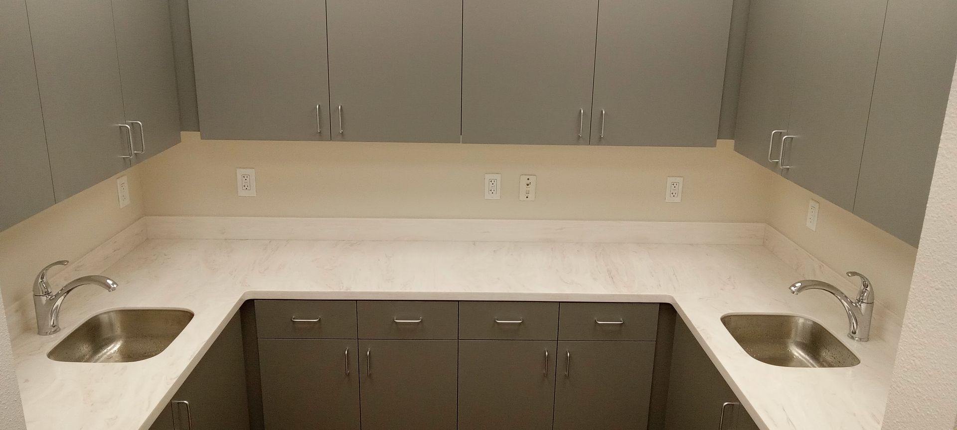 A kitchen with two sinks and gray cabinets.