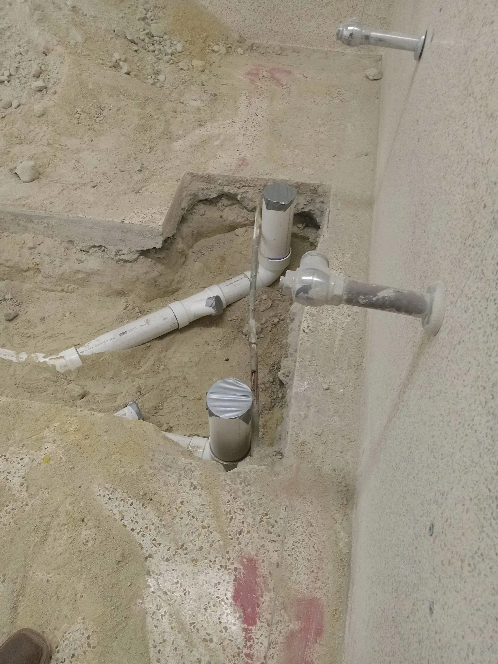 A pipe is coming out of a hole in the ground next to a wall.
