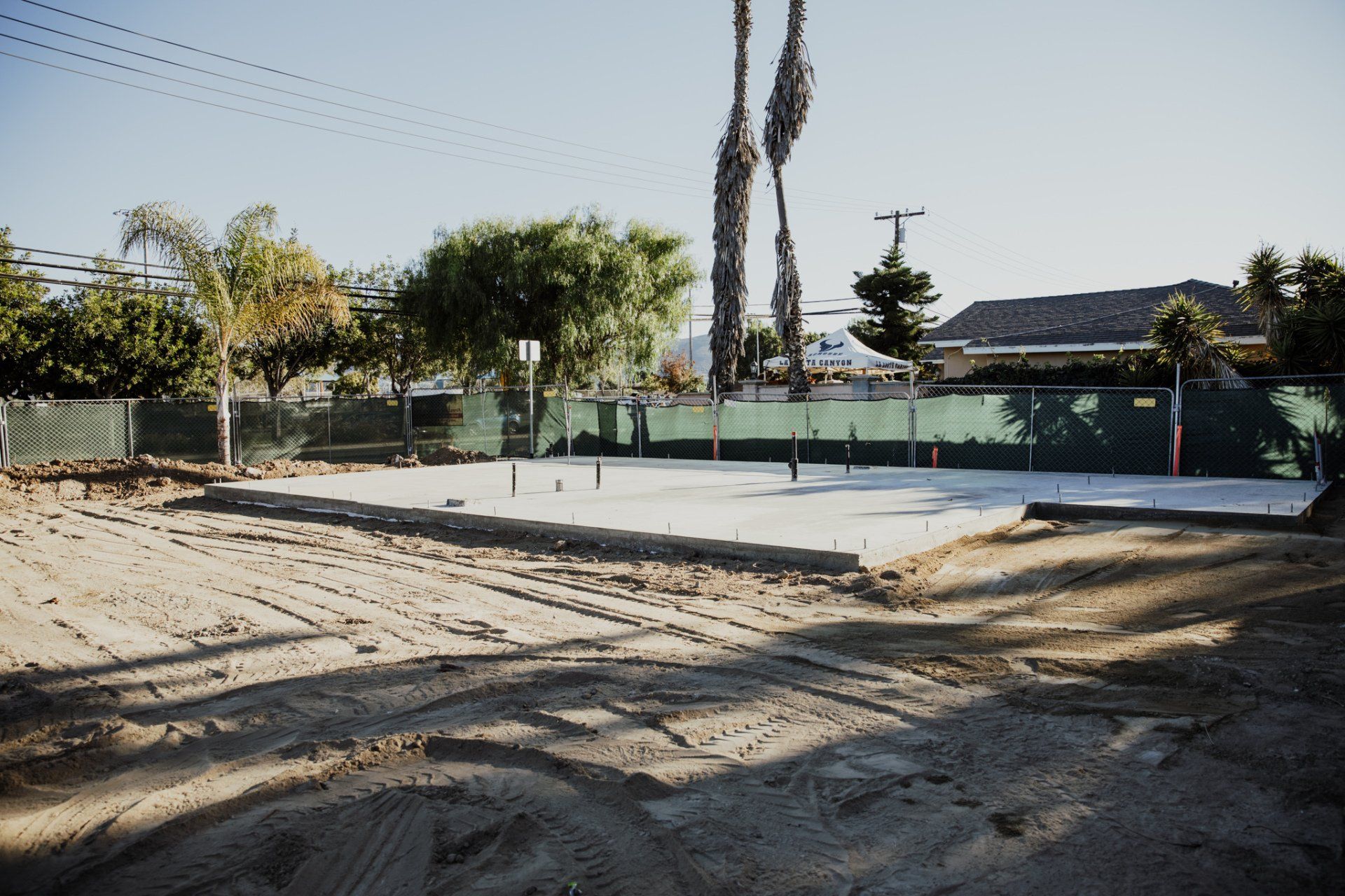 A dirt field with a fence and palm trees in the background