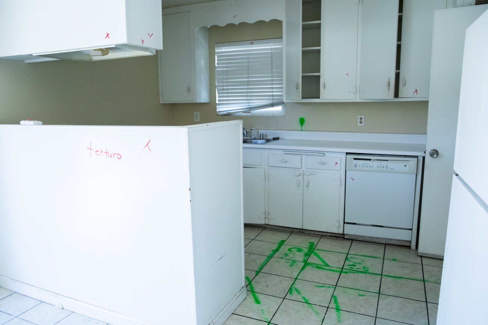 A kitchen with white cabinets and a green x on the floor
