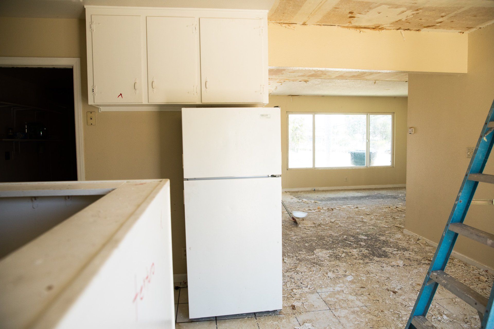 An empty kitchen with a white refrigerator and a blue ladder