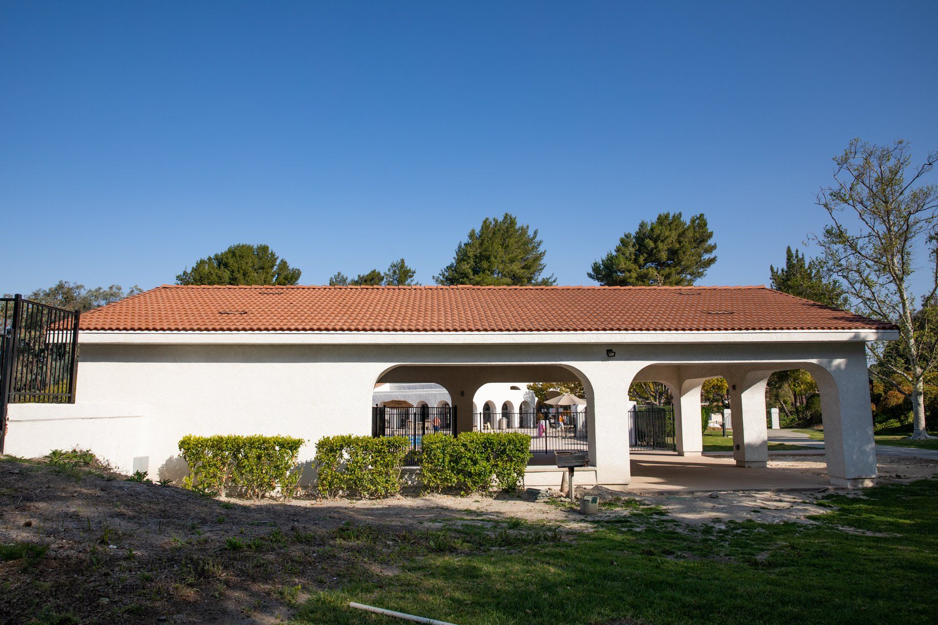 A white building with a red tile roof is surrounded by grass and trees.