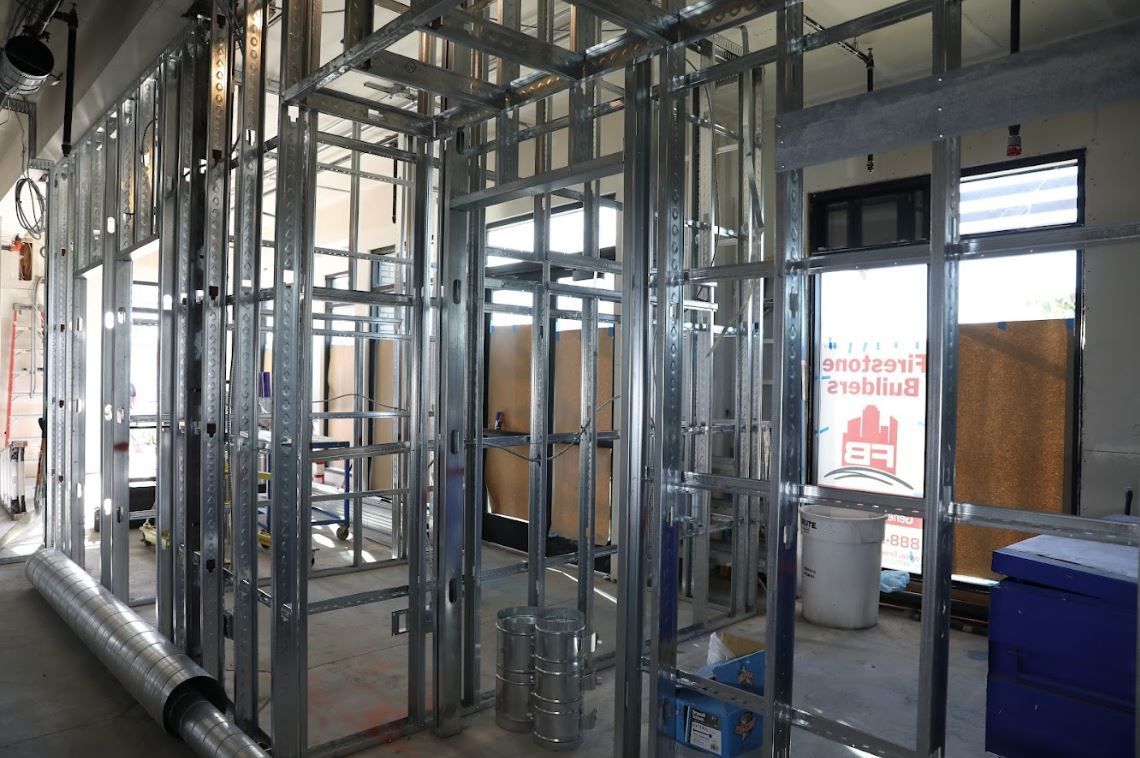 Interior under construction with exposed metal framing, glass openings, and stacked materials