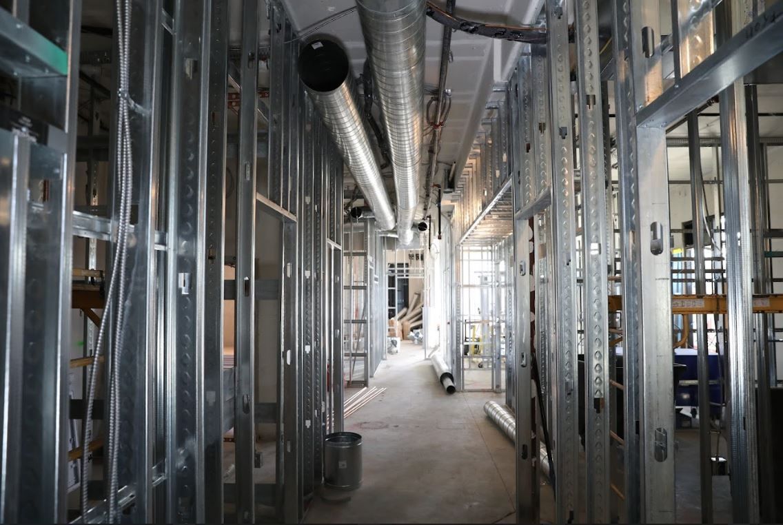 Unfinished building corridor with exposed metal studs, ducts, and a long concrete walkway