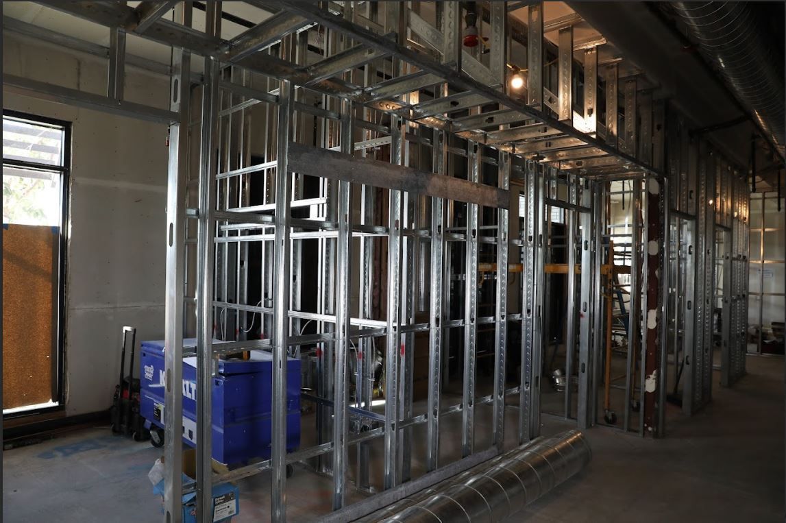 Framed metal wall structure inside an unfinished building corridor with windows and construction materials
