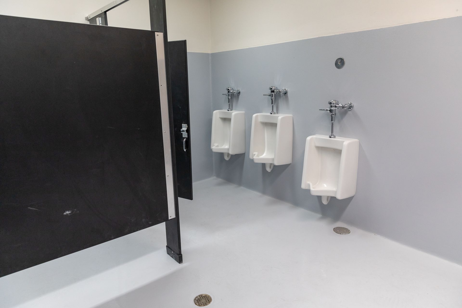 A bathroom with three urinals and a black stall