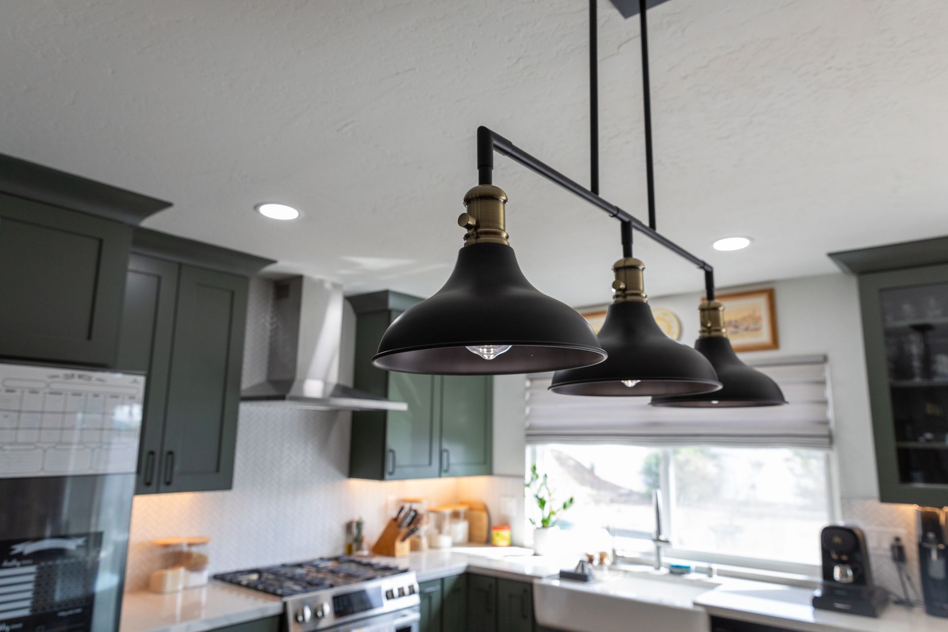 A kitchen with green cabinets and black pendant lights