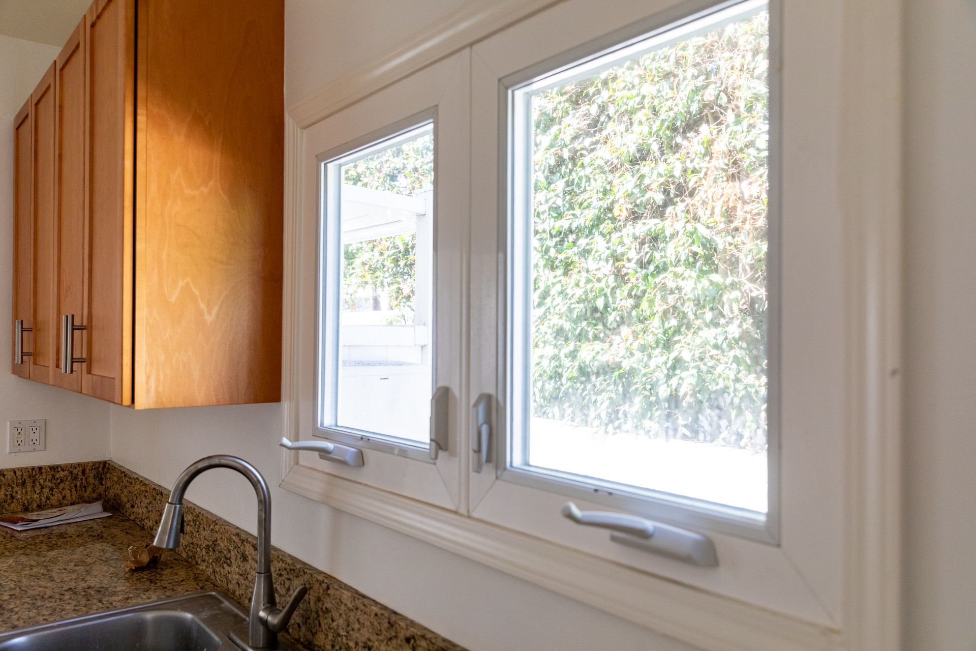 A kitchen with a sink , cabinets , and two windows.