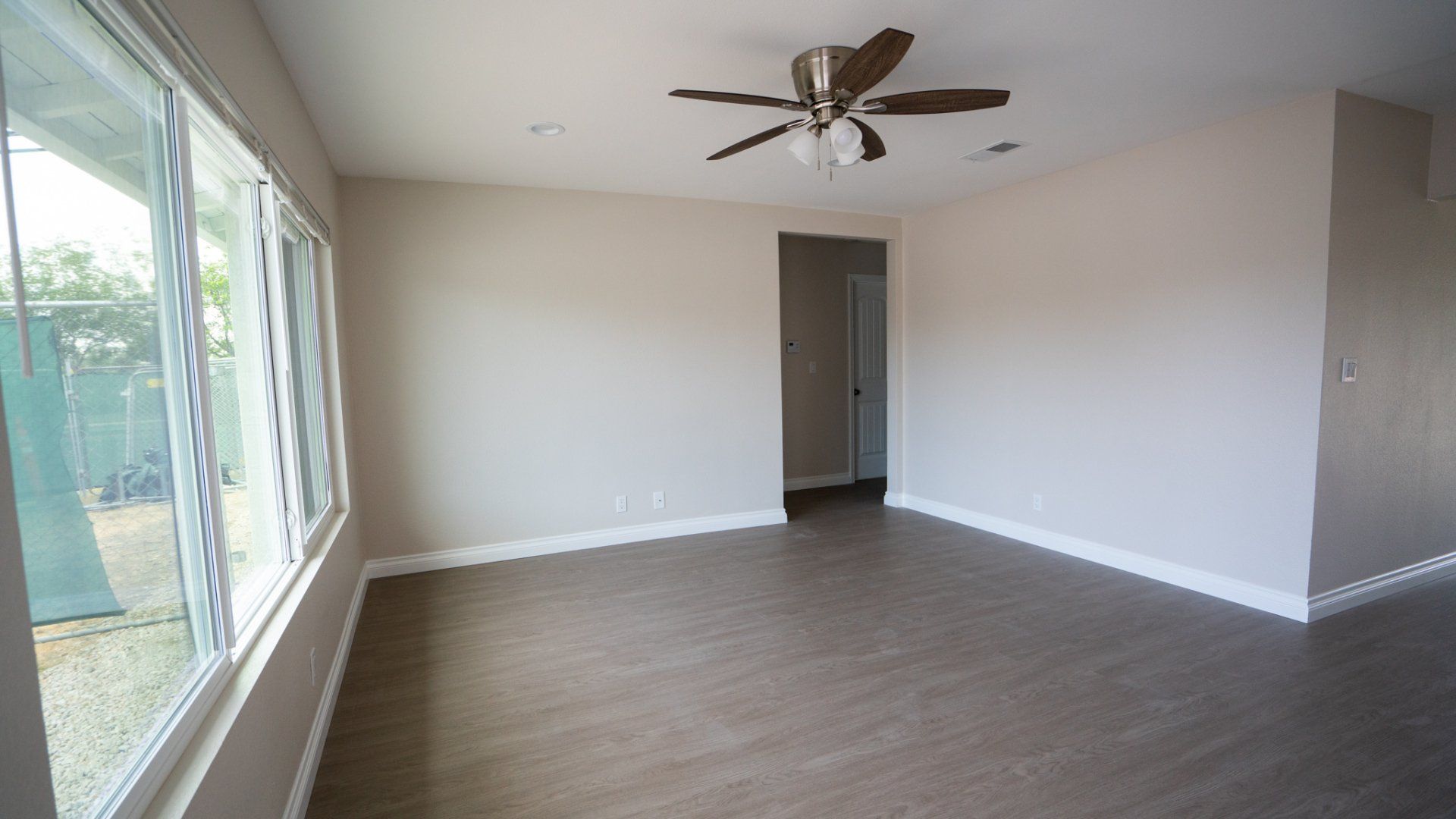 An empty living room with a ceiling fan and lots of windows