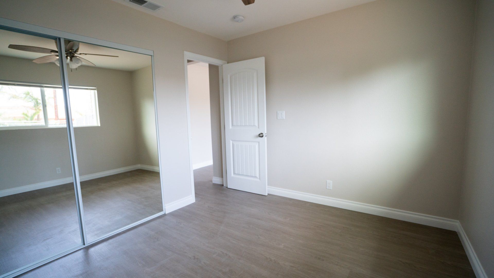 An empty bedroom with a large mirror and a ceiling fan
