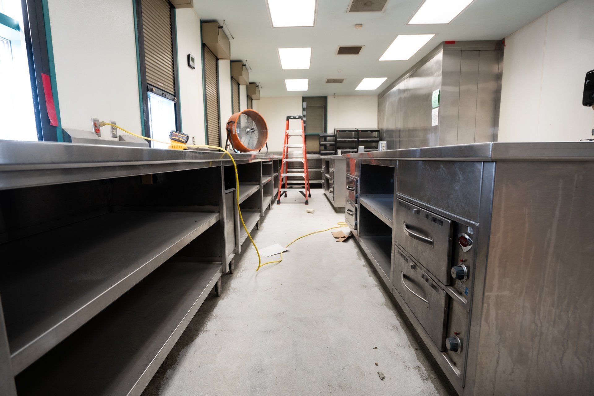 An empty kitchen with a ladder and a fan on the floor