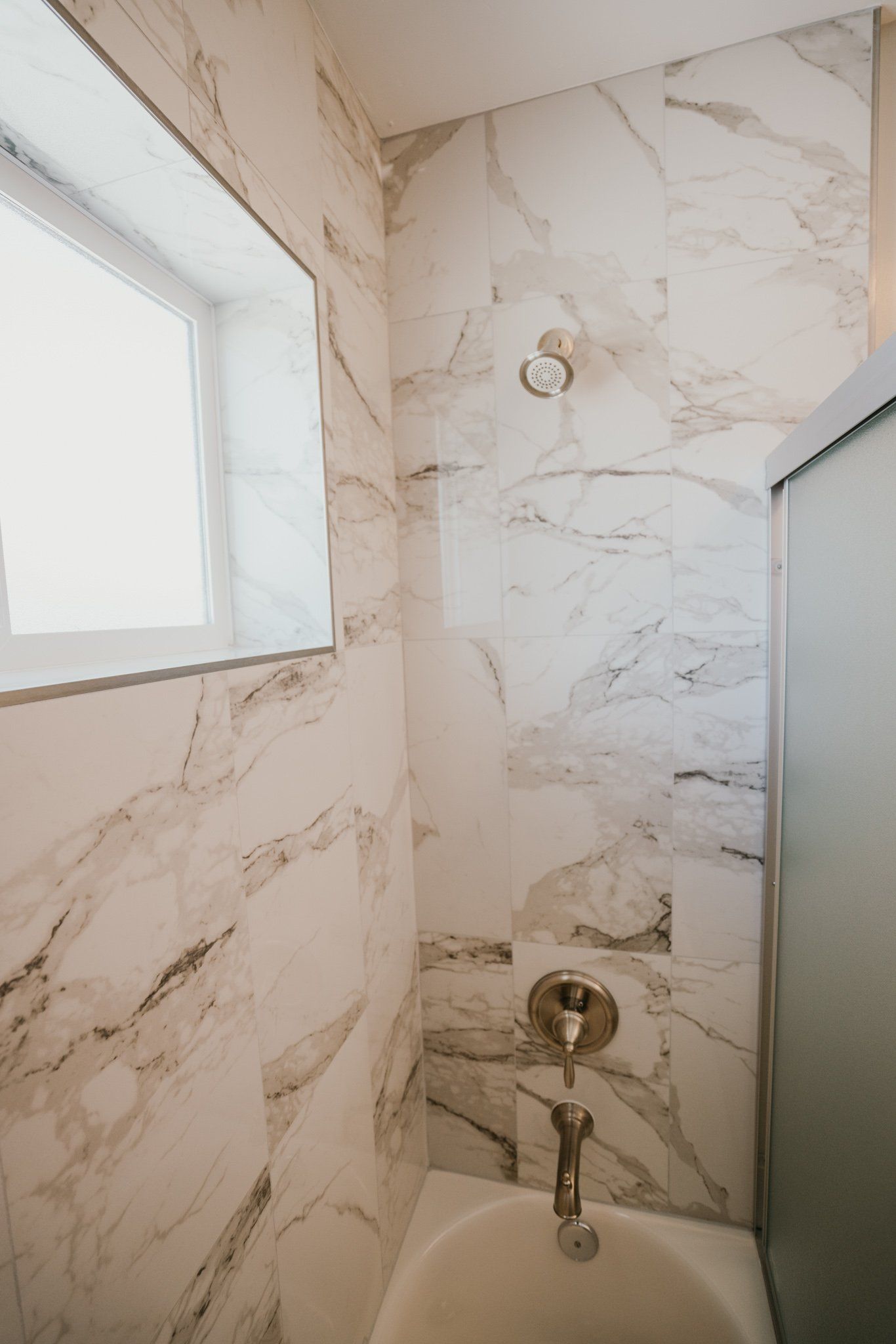 A bathroom with marble tiles , a tub and a shower.
