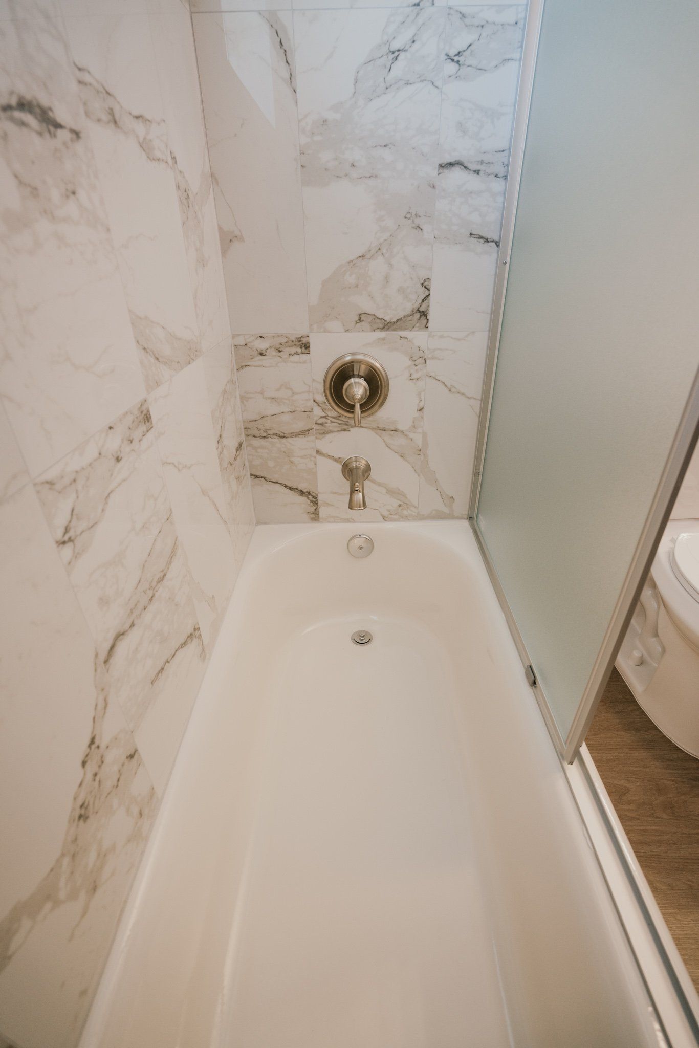 There is a bathtub in the bathroom with marble walls.