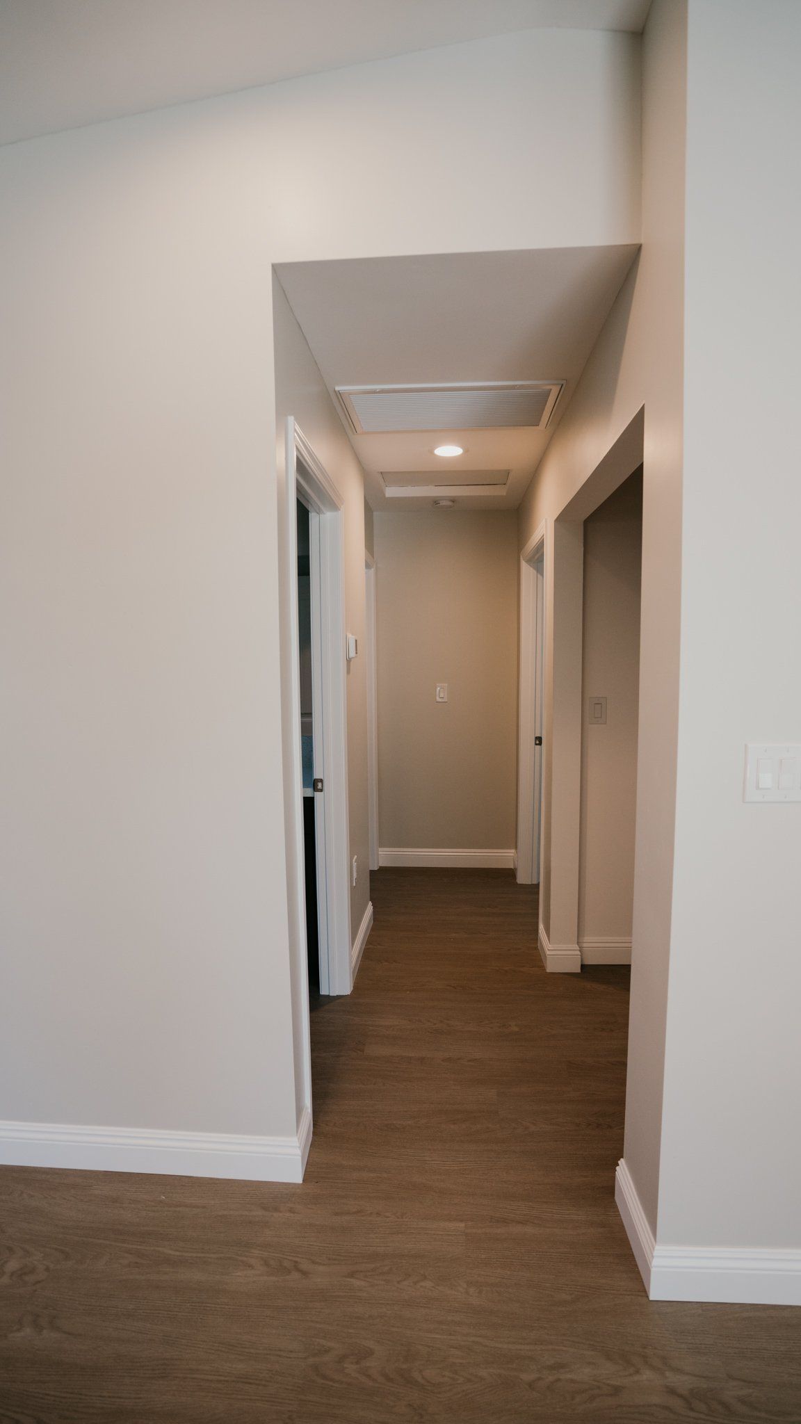 A long hallway in a house with a carpeted floor and white walls.