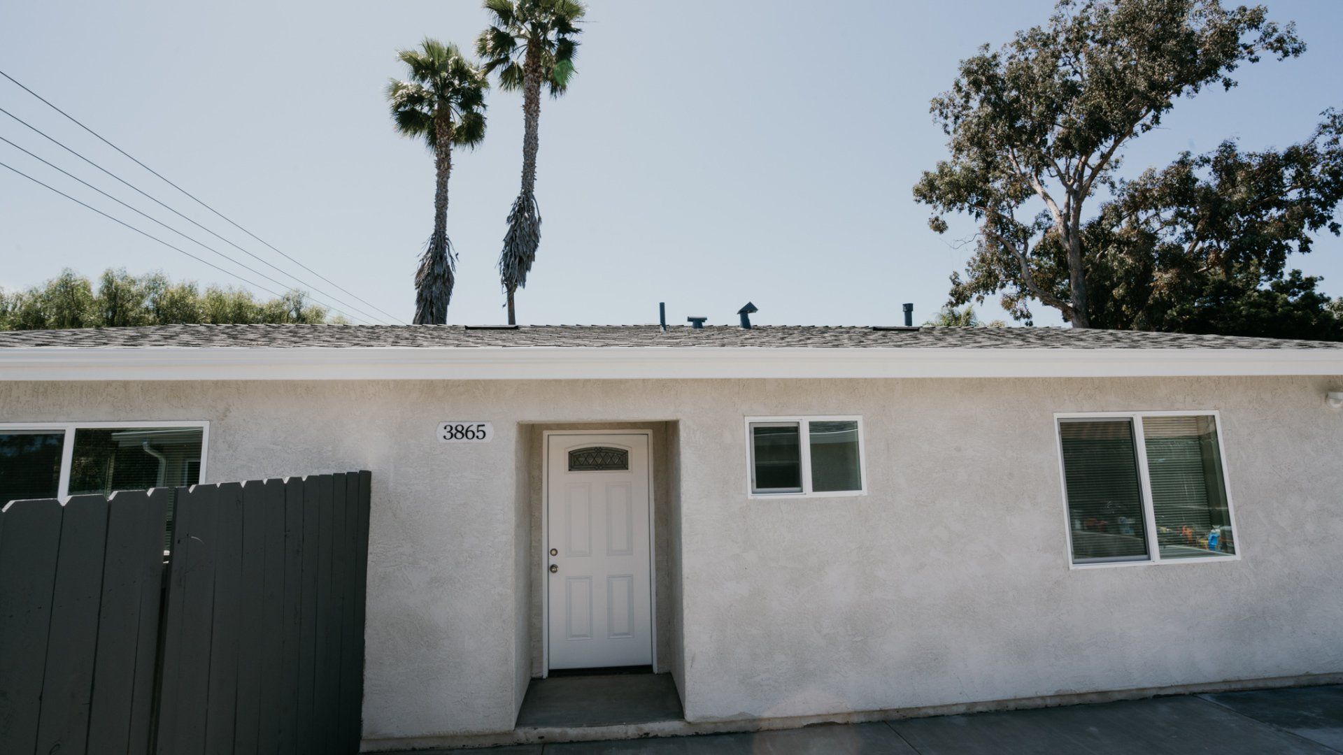 A white house with a black fence and palm trees in the background.