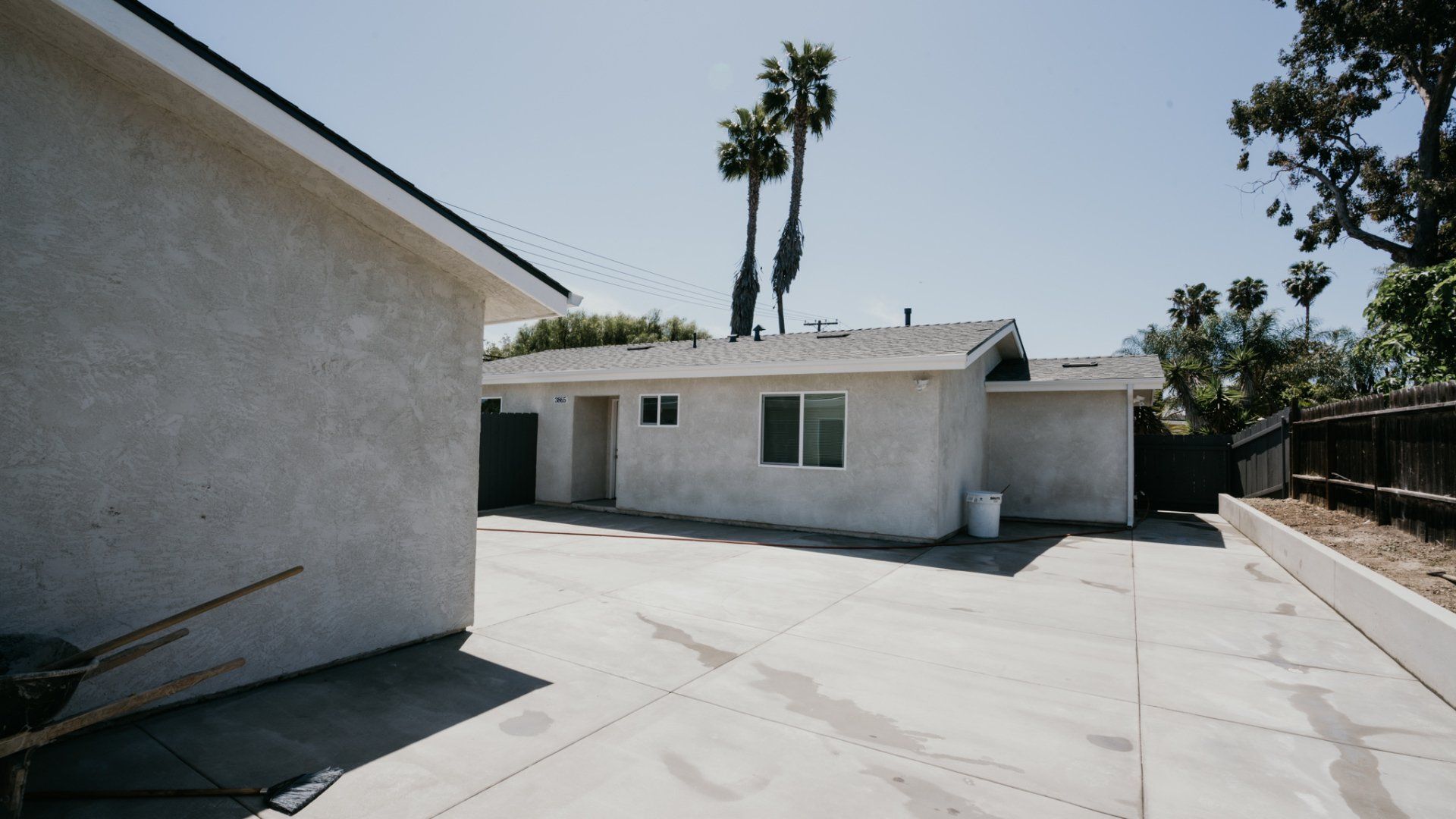 A concrete driveway leading to a house with palm trees in the background