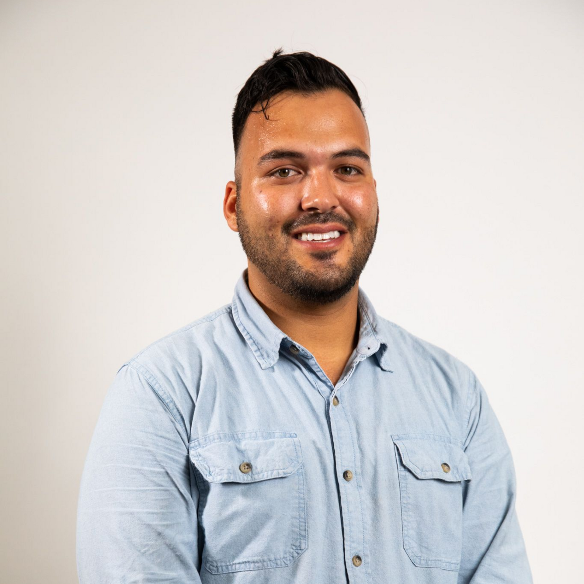 Smiling man in a light blue button-up shirt against a plain white background