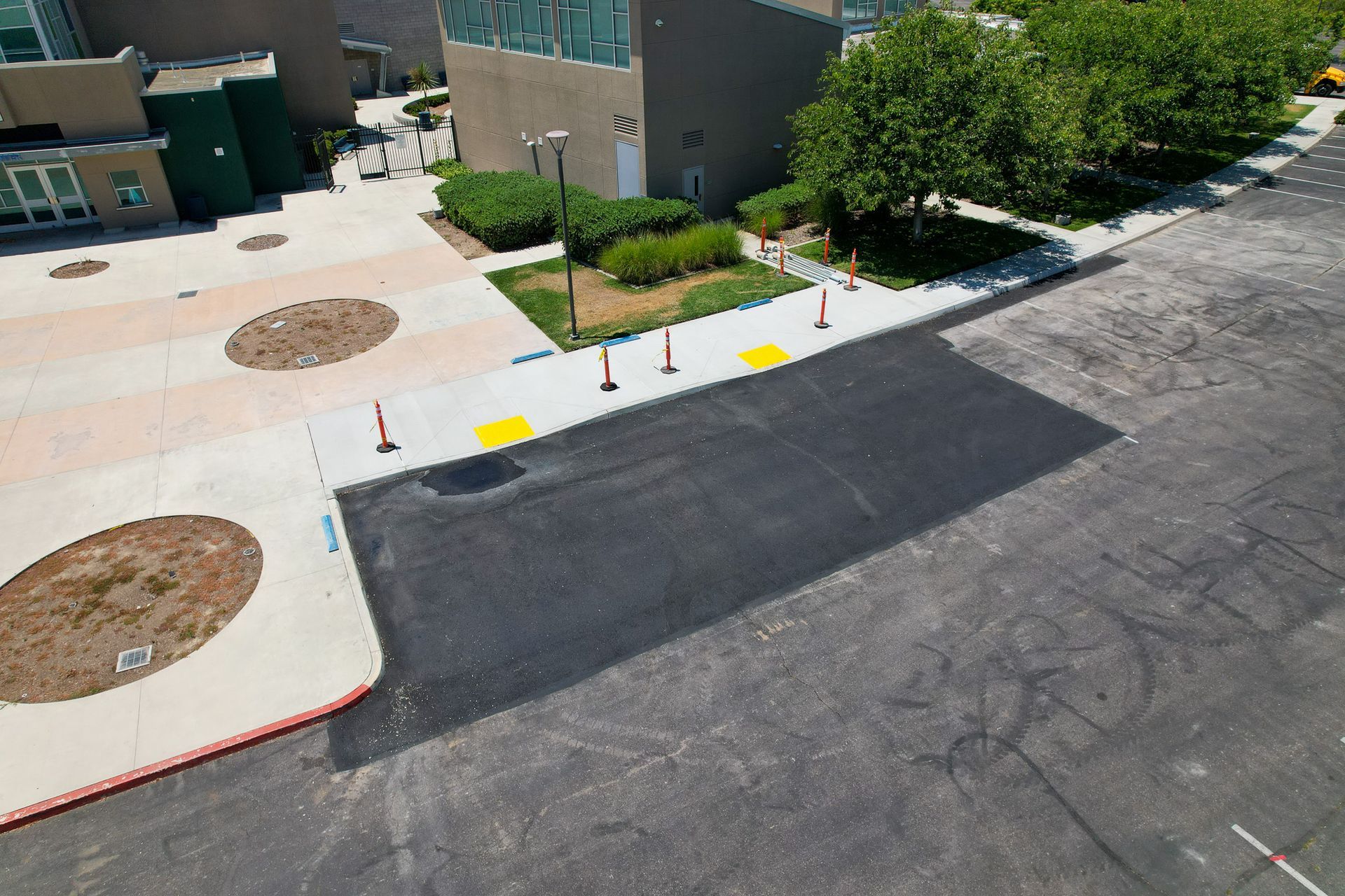 New asphalt curb ramp beside a sidewalk, with cones and painted curb markings near a building.