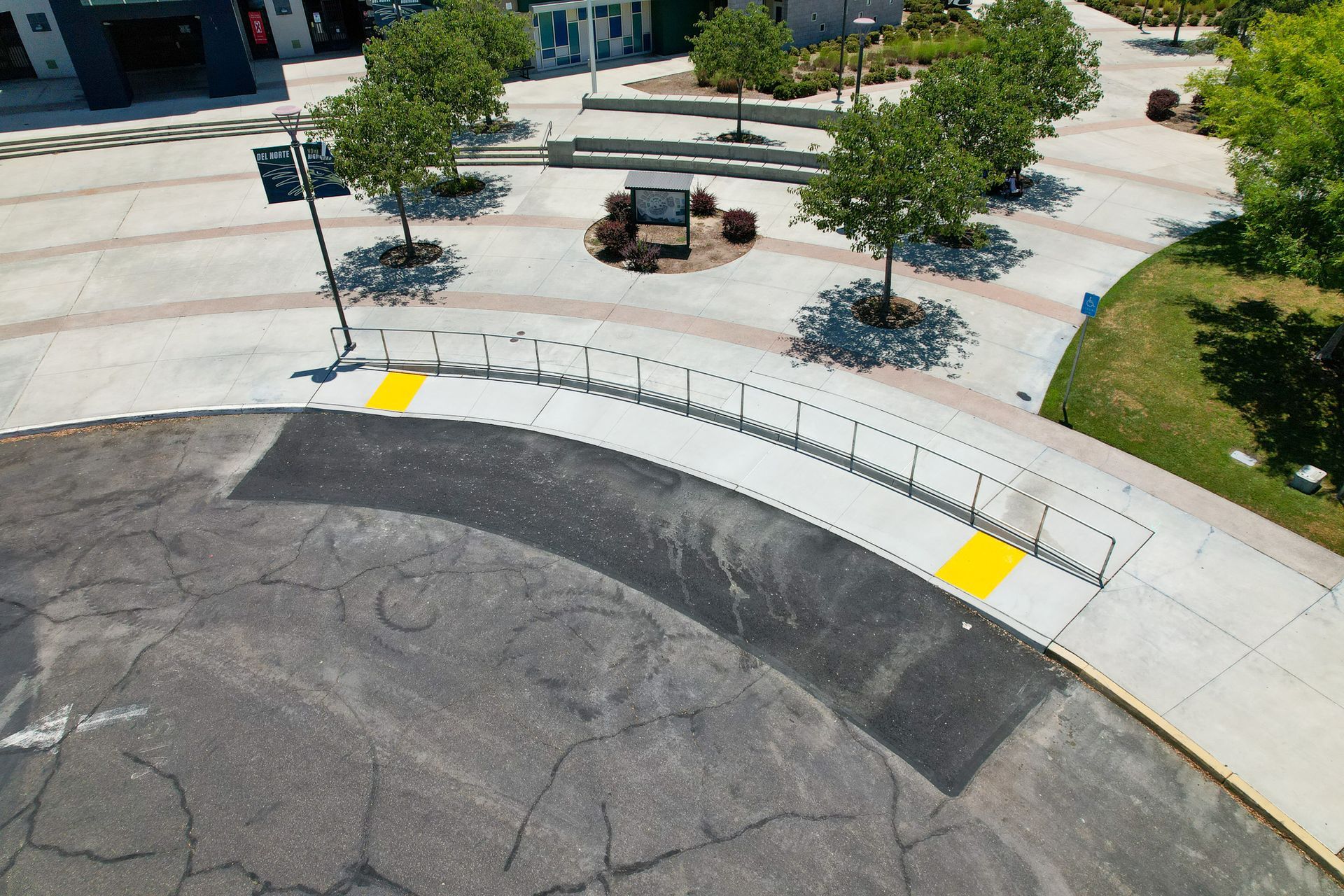 Aerial view of a curved sidewalk with yellow tactile paving and benches in a plaza.