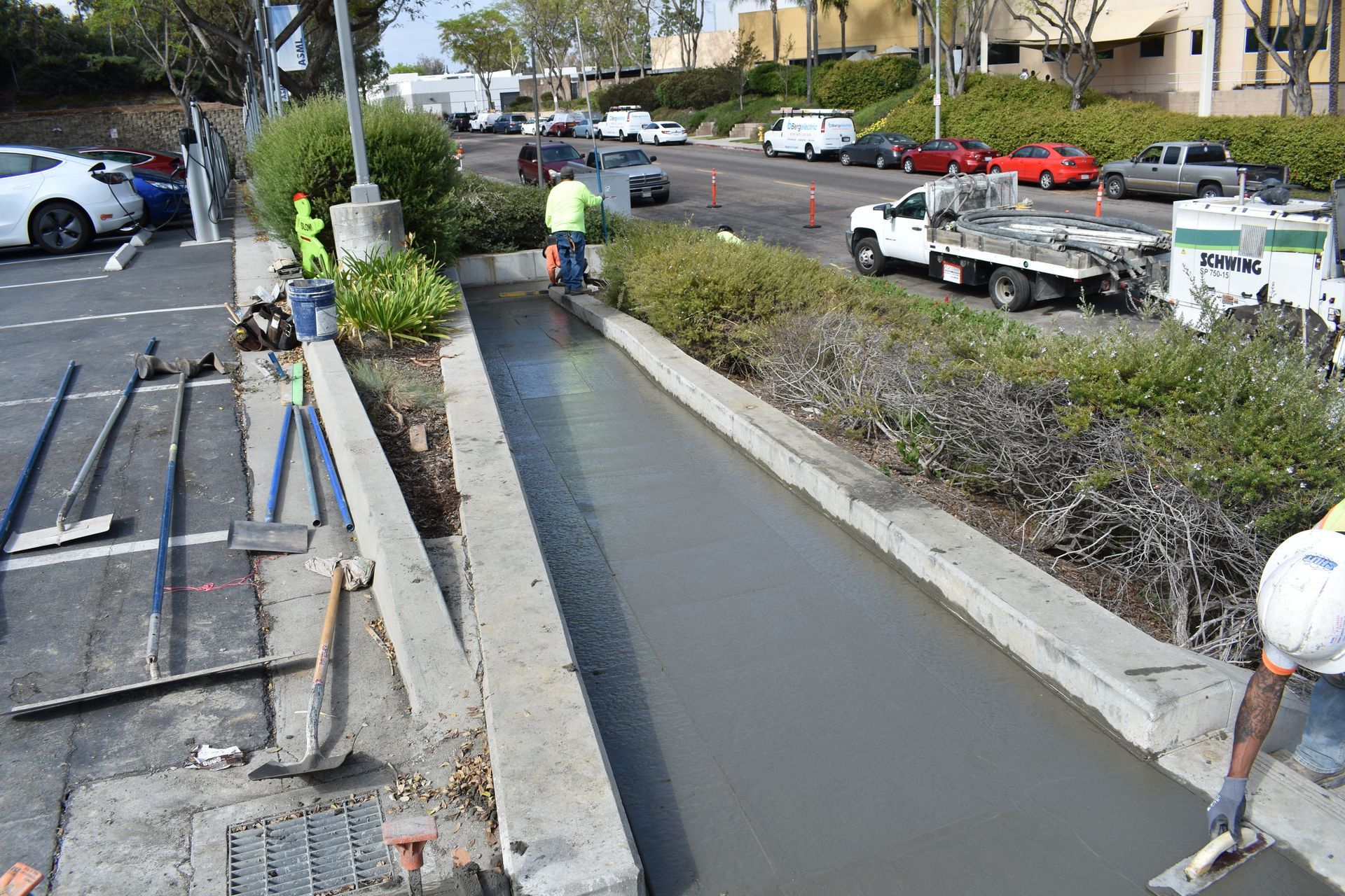 A man is spreading concrete on a sidewalk in a parking lot.