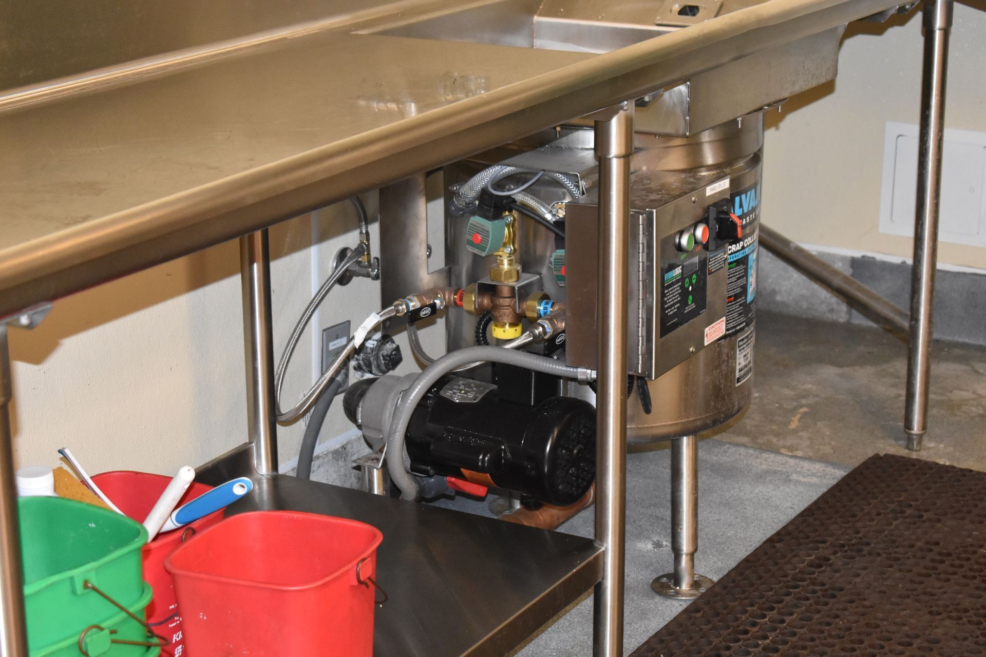 A stainless steel sink with a motor and buckets underneath it.