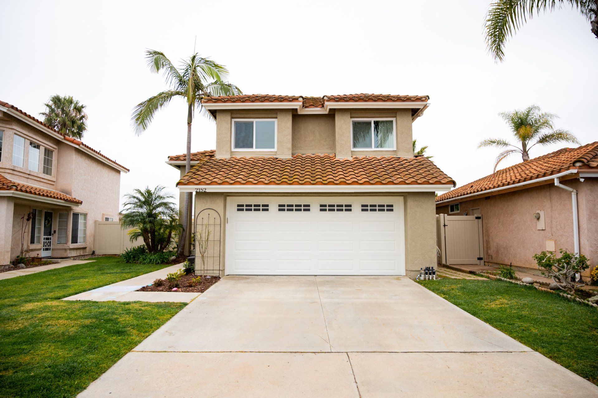 A house with a white garage door and a palm tree in front of it.