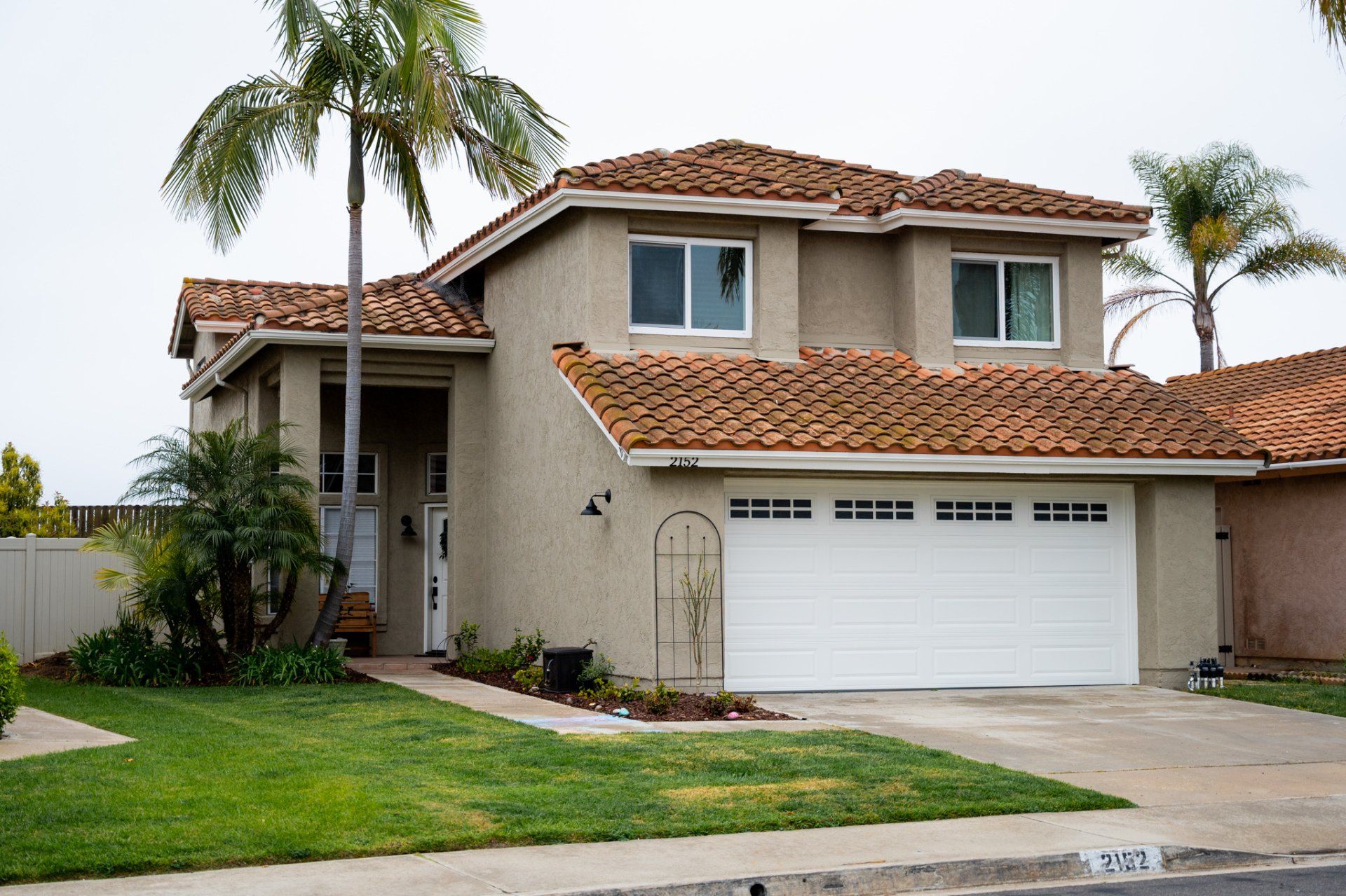 A house with a white garage door and a palm tree in front of it