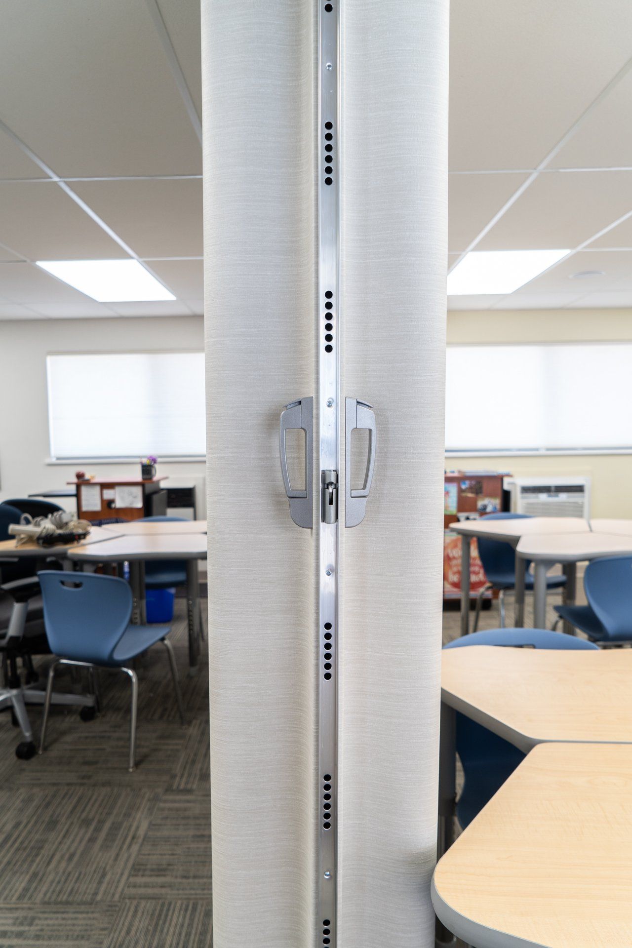 A classroom with tables and chairs and a hand sanitizer dispenser on the wall.