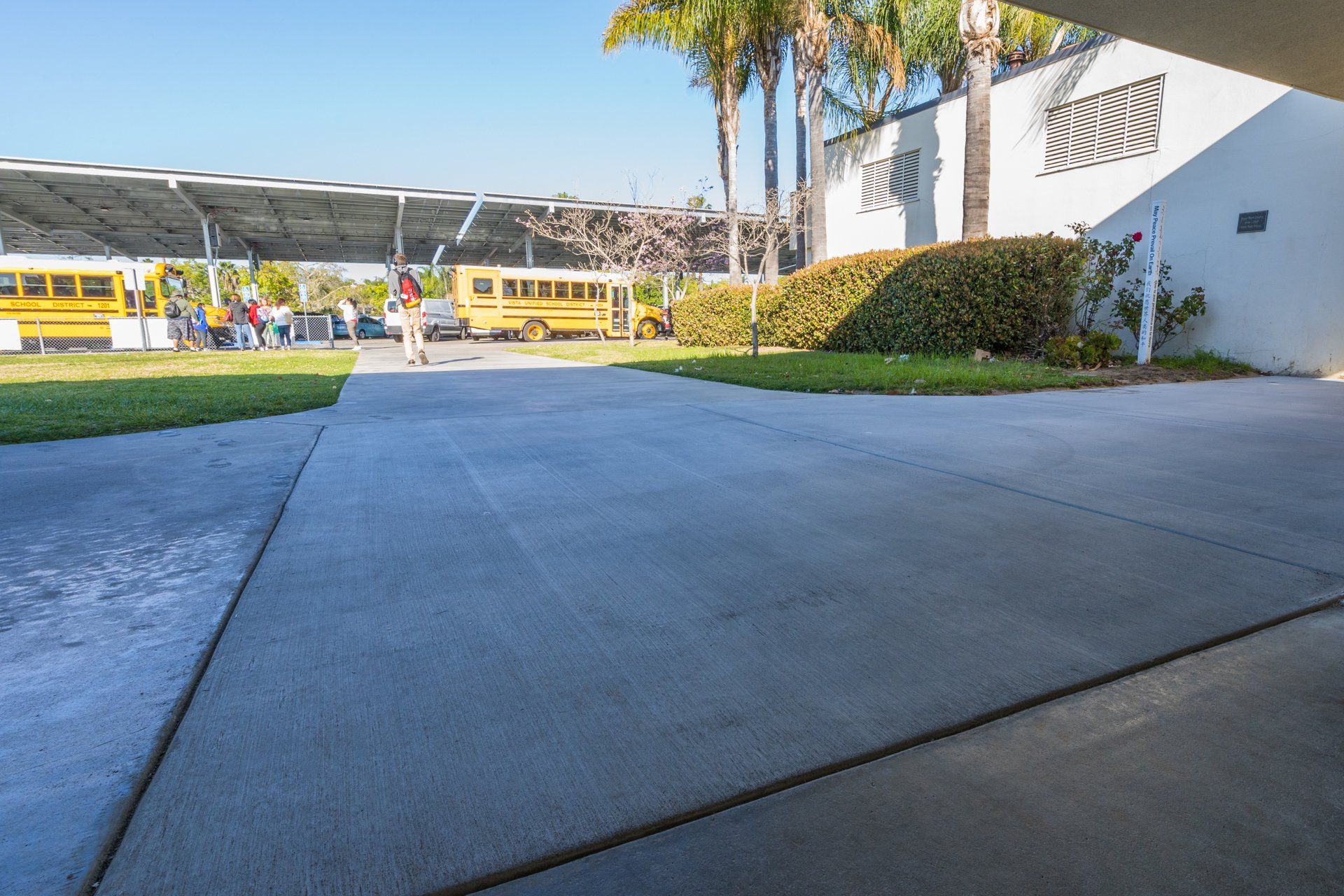 A person is walking down a sidewalk in front of a school bus.