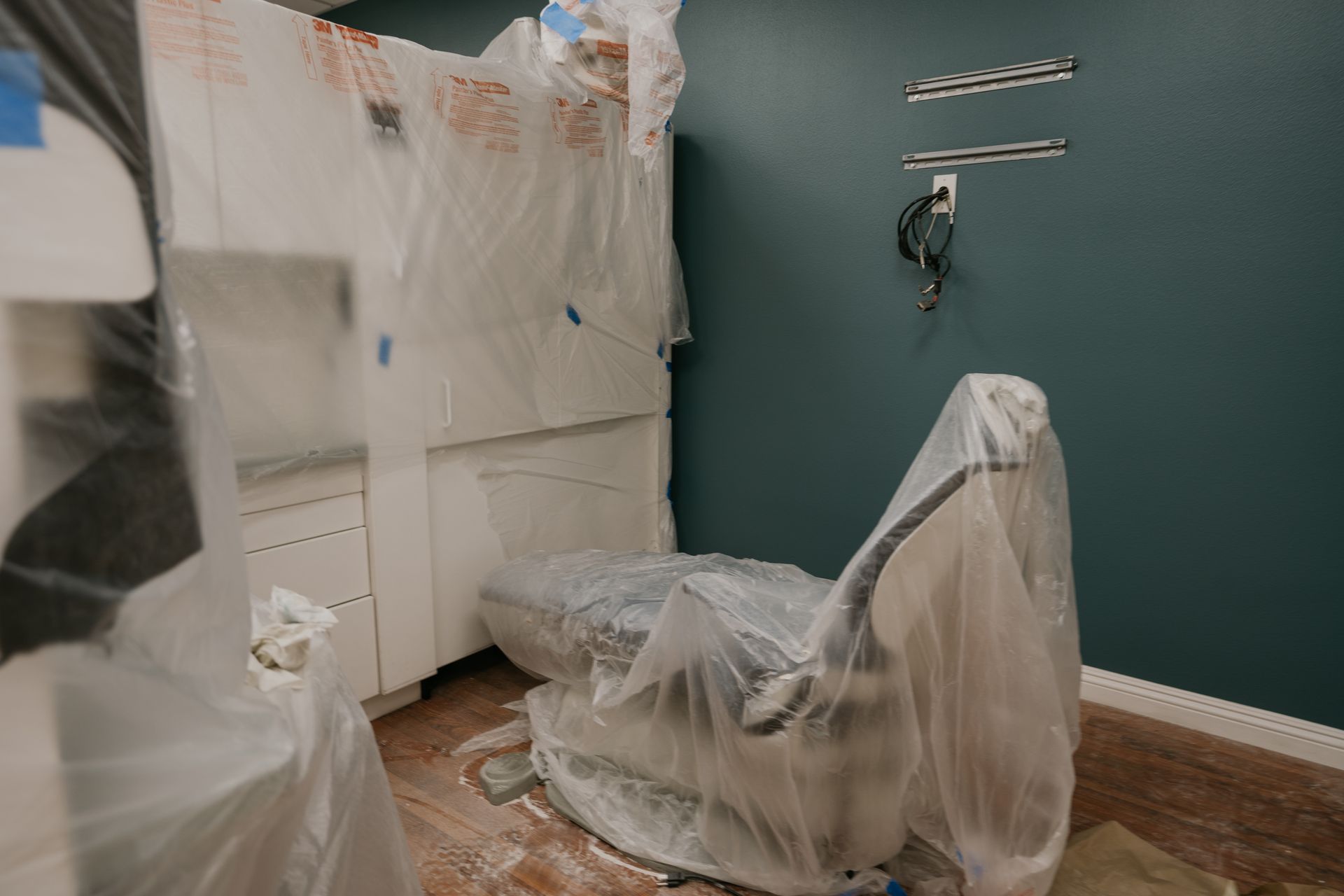 A dental chair is wrapped in plastic in a room under construction.