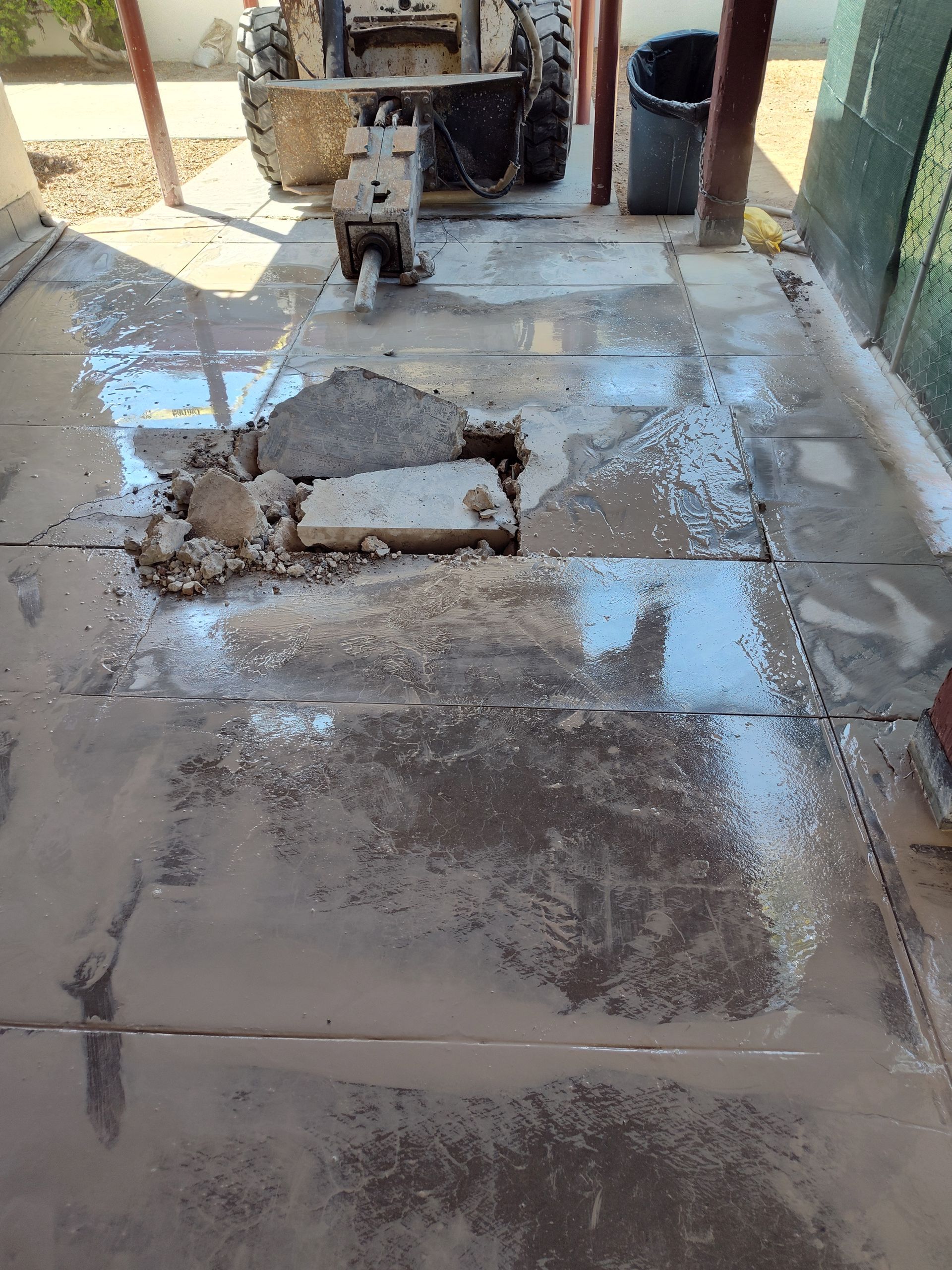 A concrete floor with a hole in it and a bulldozer in the background.