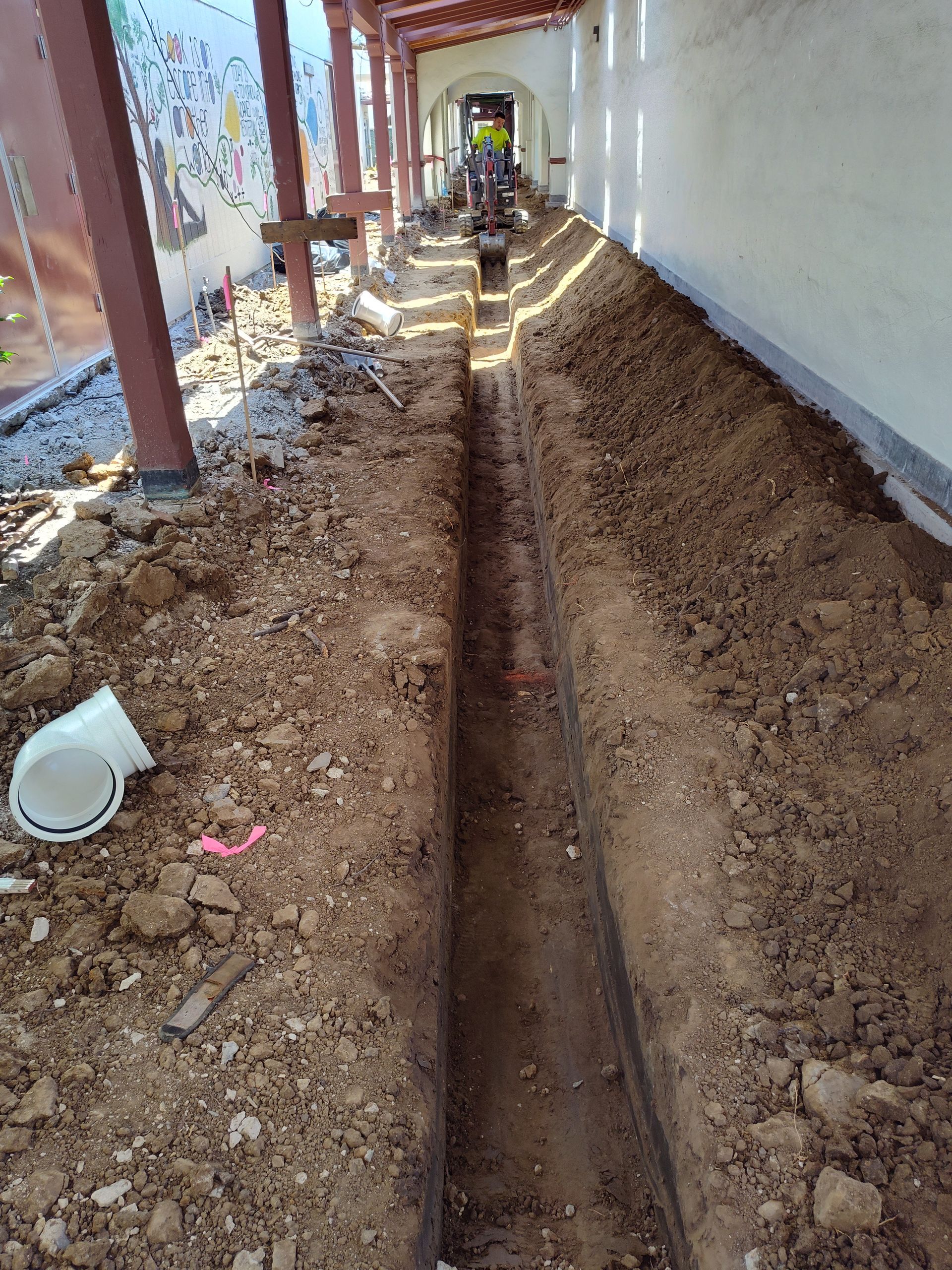 A person is digging a trench in the dirt next to a building.