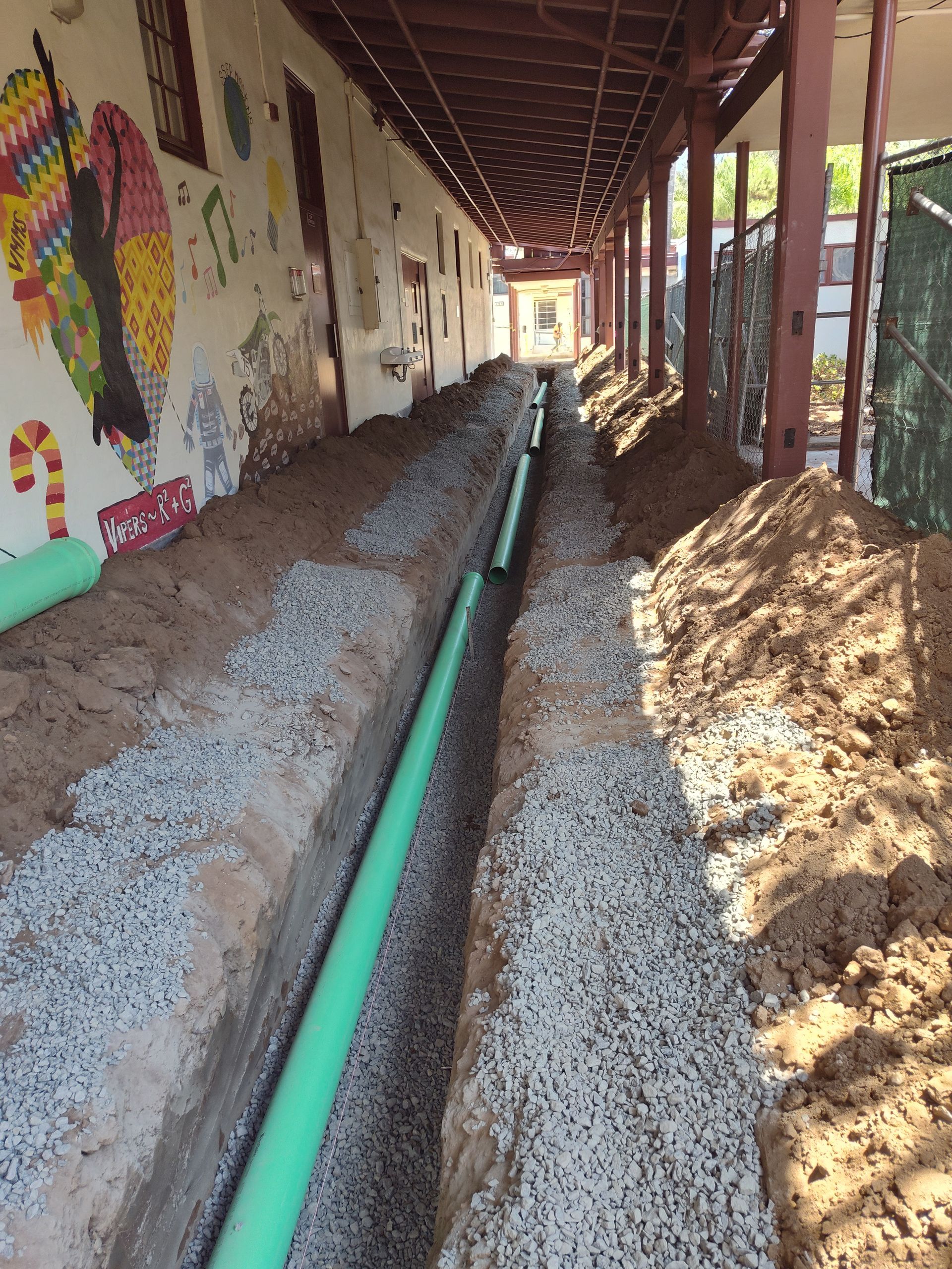 A green pipe is being installed in the dirt in a hallway