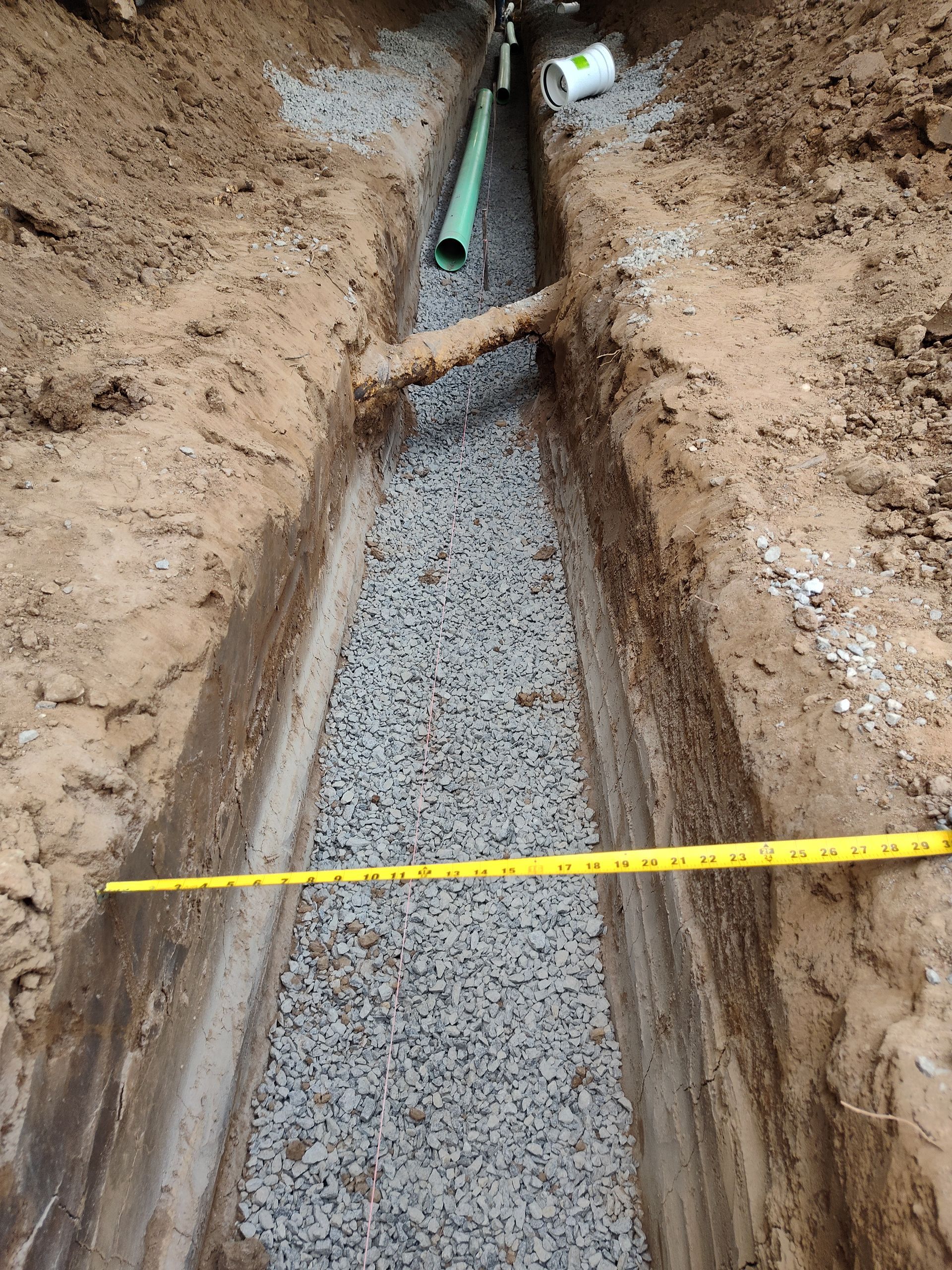 A yellow tape measure is being used to measure a pipe in a trench.