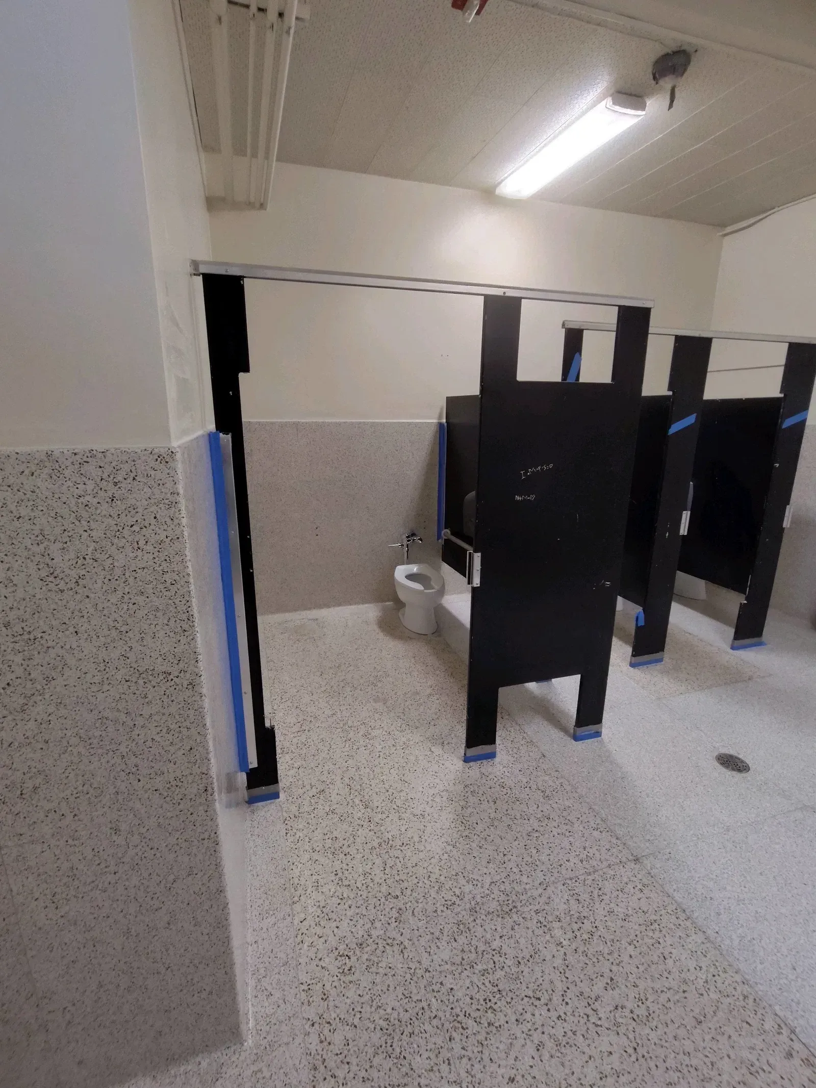 A bathroom with black stalls and a toilet.
