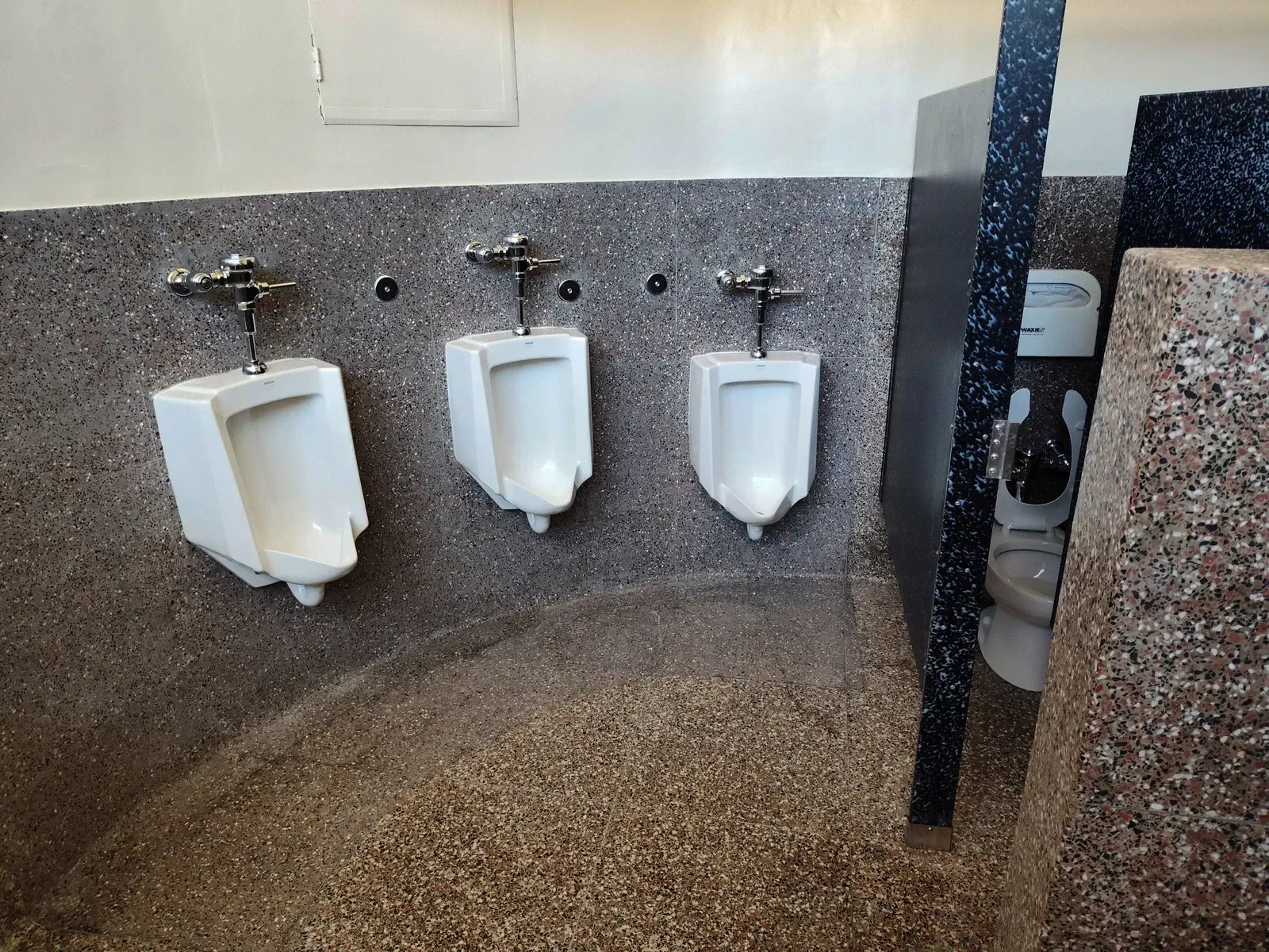 A public restroom with three urinals and a toilet