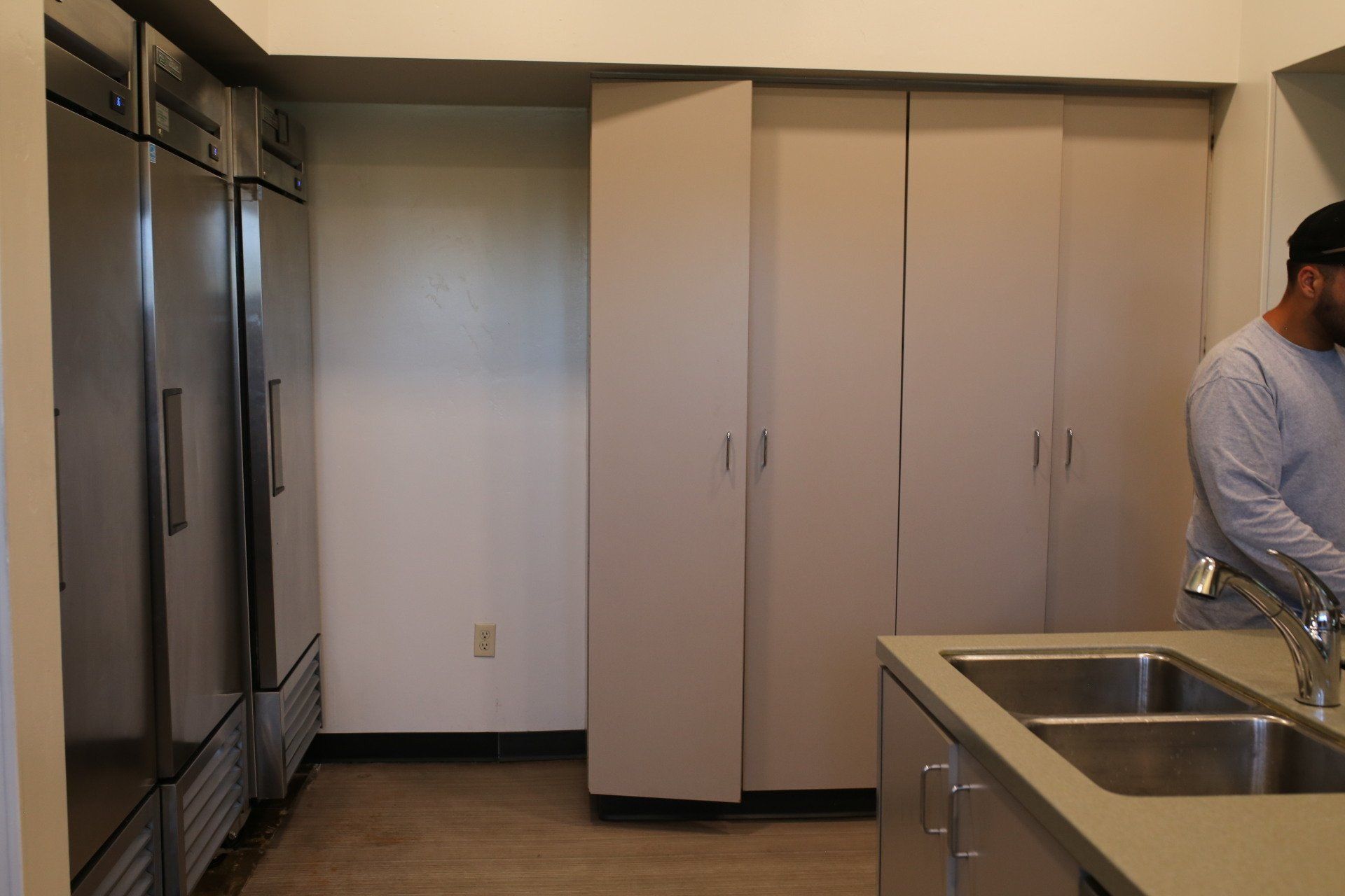 A man in a kitchen with a sink and refrigerators