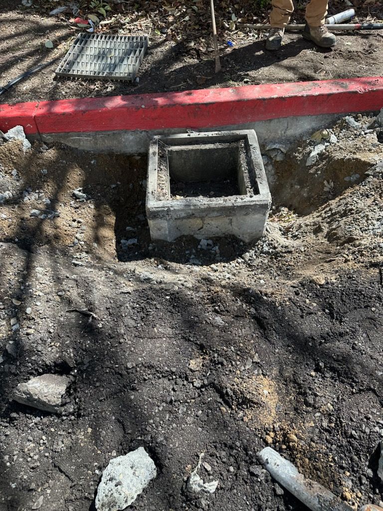 A manhole cover is being installed in the dirt next to a red curb.