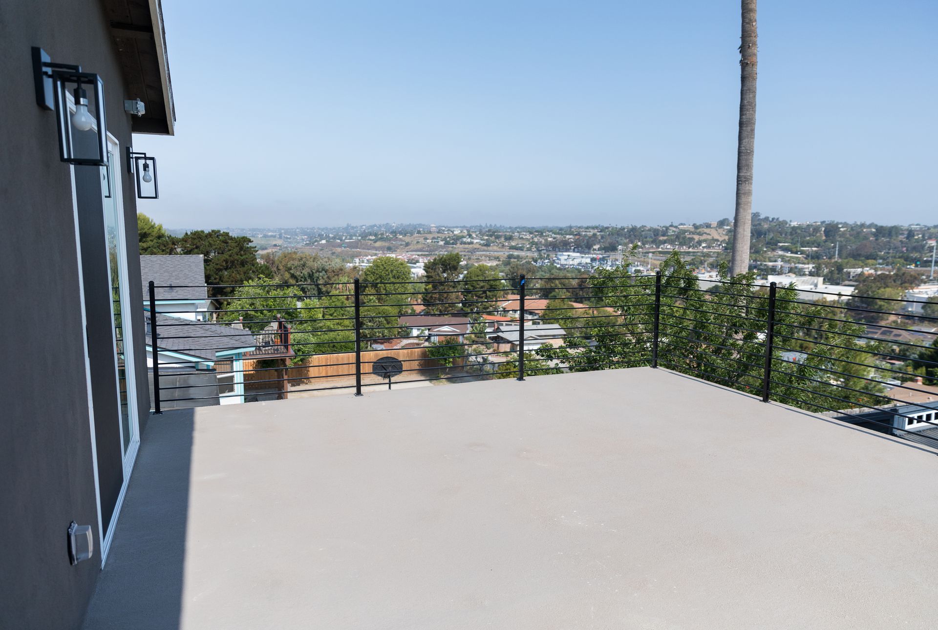 A balcony with a view of a city and a palm tree.
