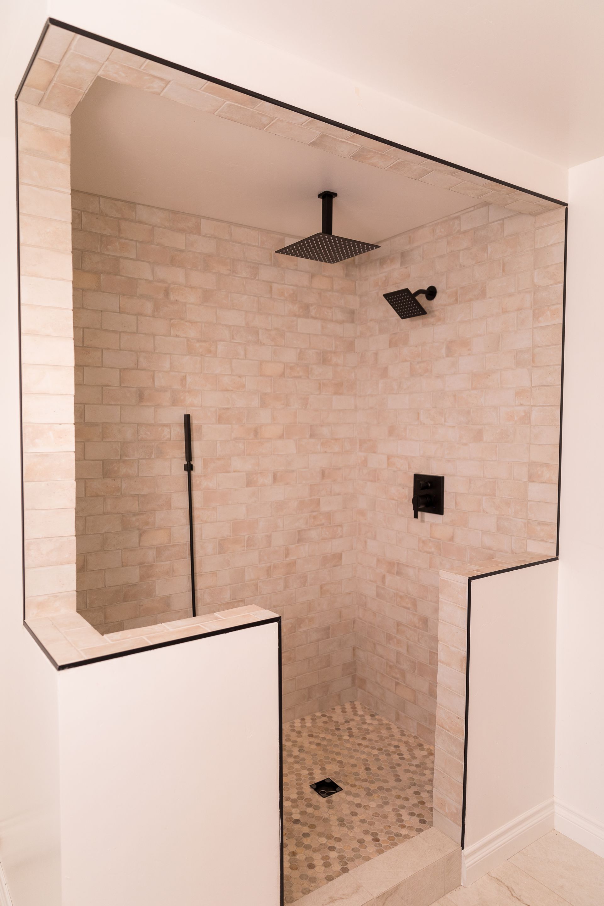 A bathroom with a walk in shower with a brick wall and a glass door.