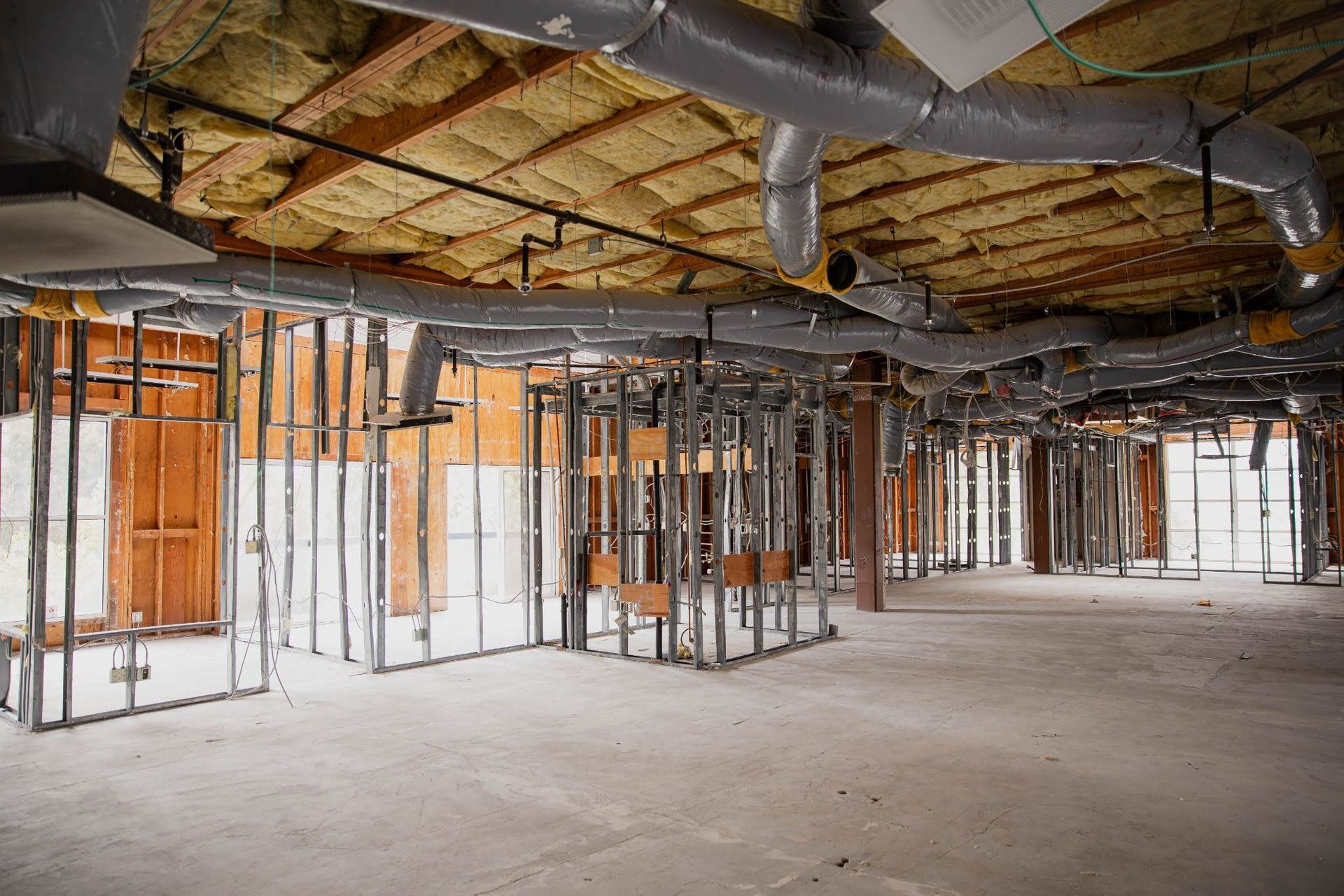 Interior of a building under construction with exposed framing, ductwork, and unfinished ceiling insulation