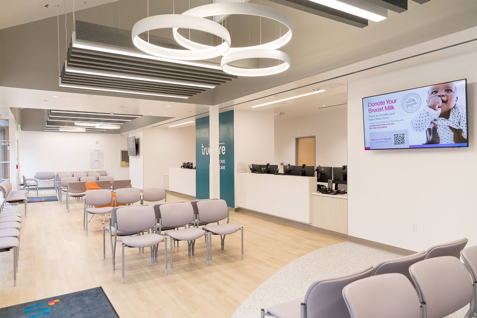 Modern waiting room with rows of chairs, wall TV, and circular ceiling lights
