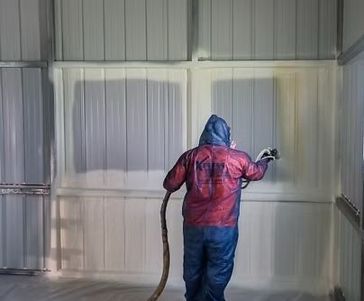Person in protective suit spraying insulation foam on interior metal walls.