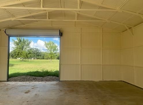 Inside a beige metal-walled garage, open door reveals a green field and trees under a blue sky.